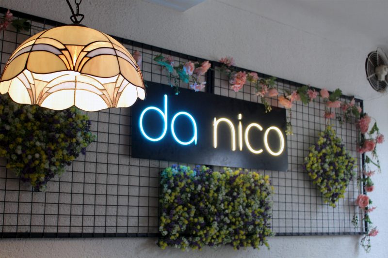 Das Leuchtschild da nico an der Blumenwand